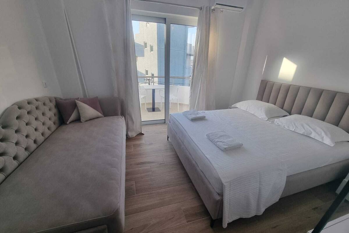 A hotel room with a sofa, a bed, and a balcony with a view of buildings.
