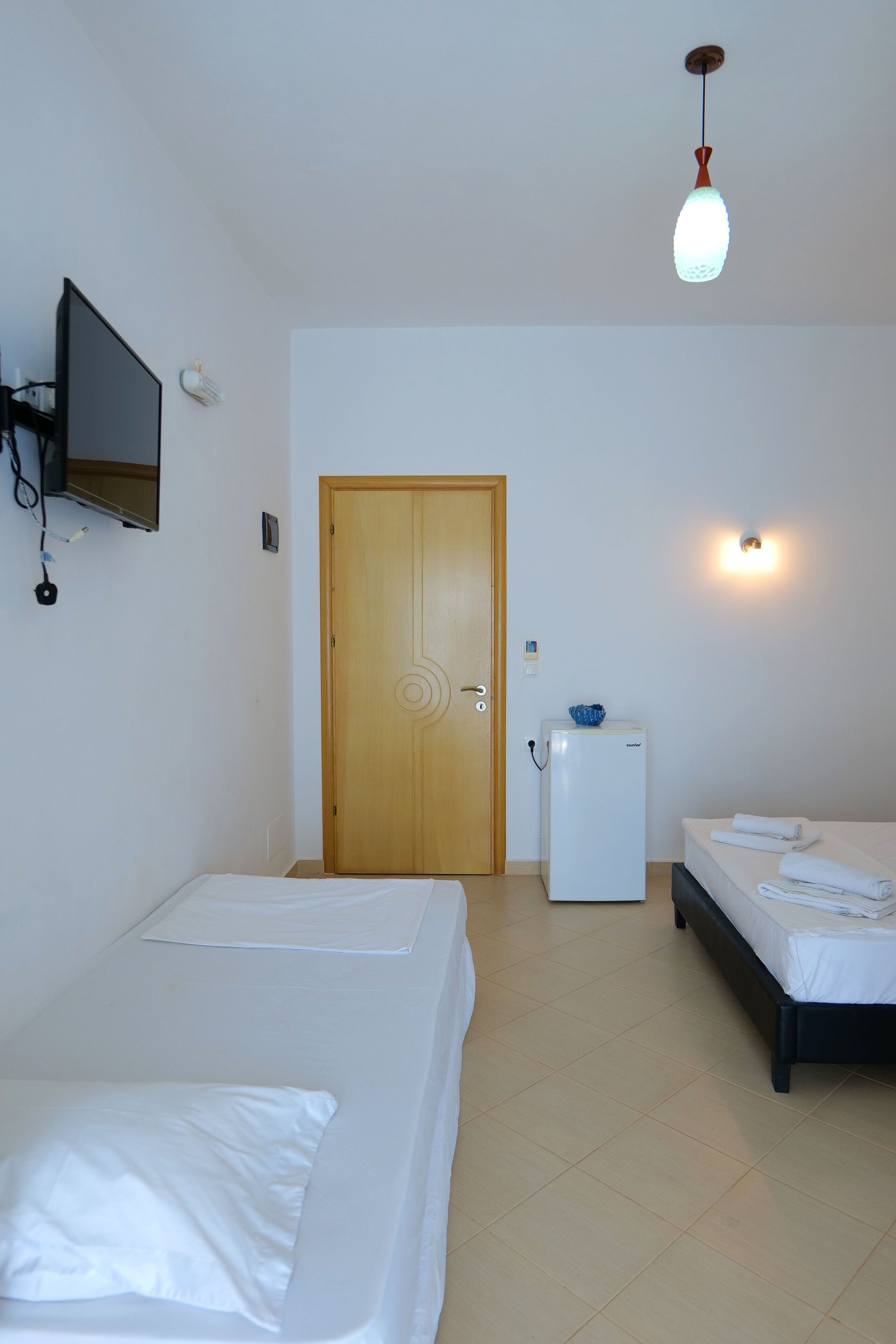A hotel room with two beds, a refrigerator, a television mounted on the wall, and a door.