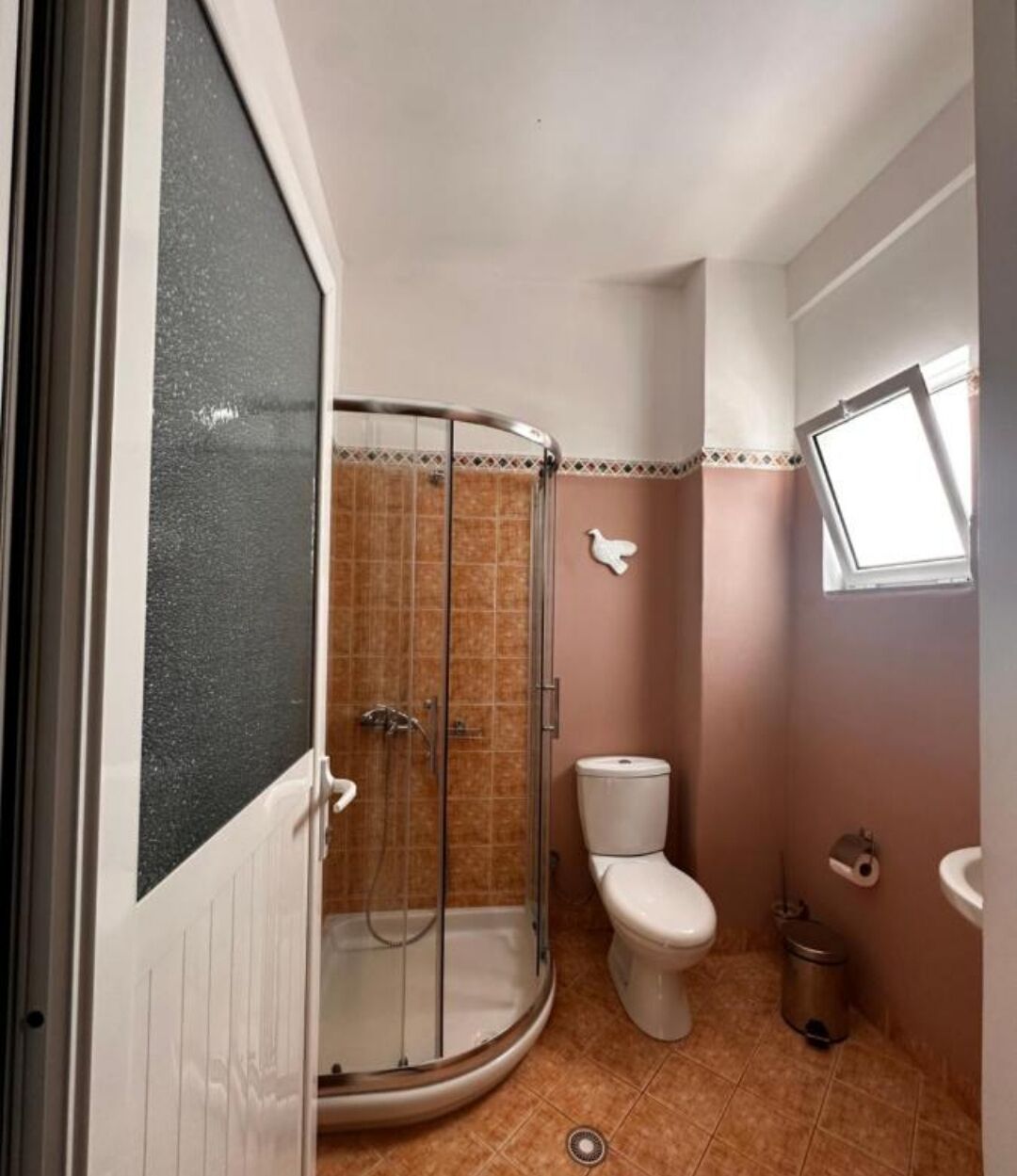 A bathroom with a glass-enclosed shower, a toilet, and a sink.