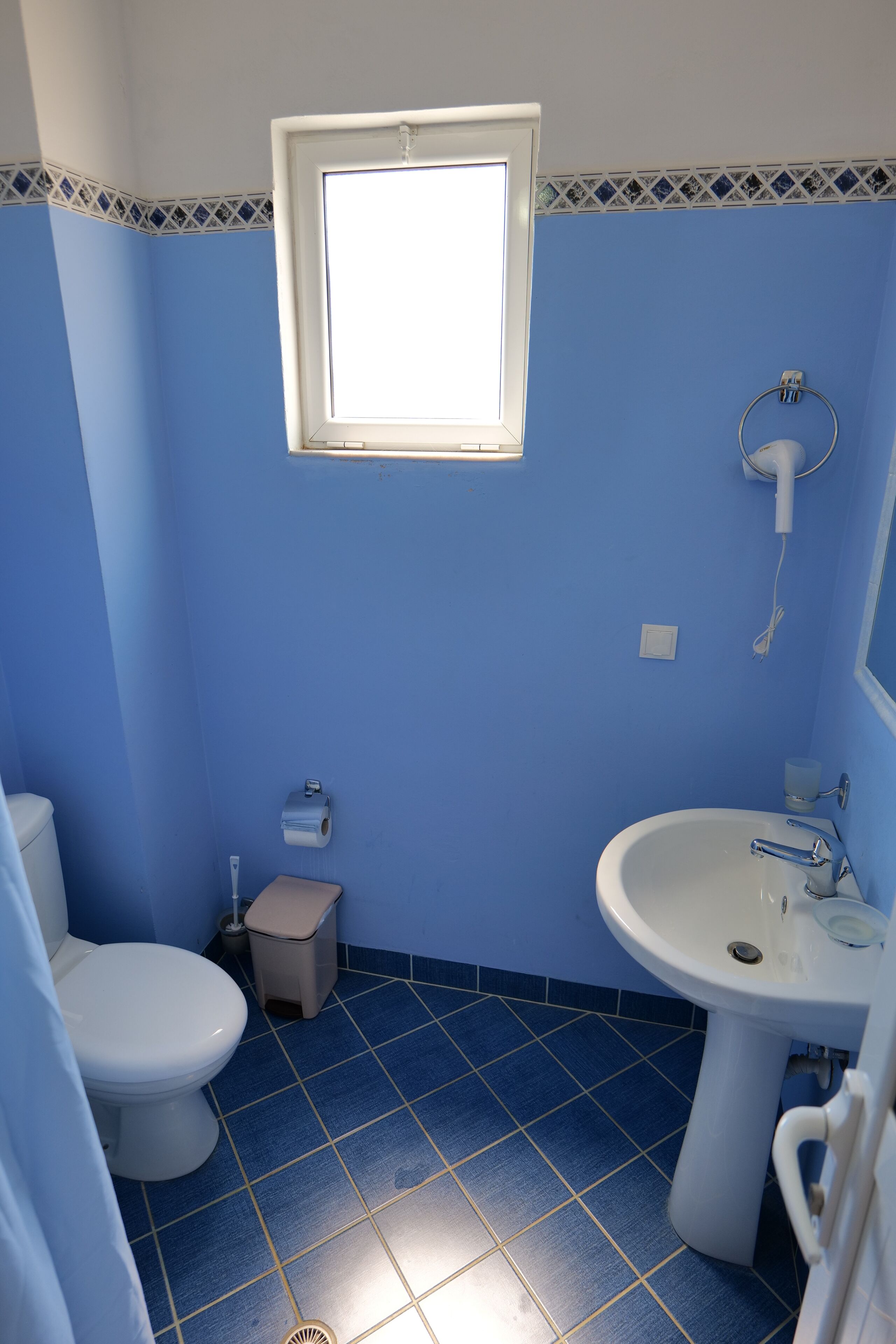 A bathroom with a toilet, sink, and a window above the sink.