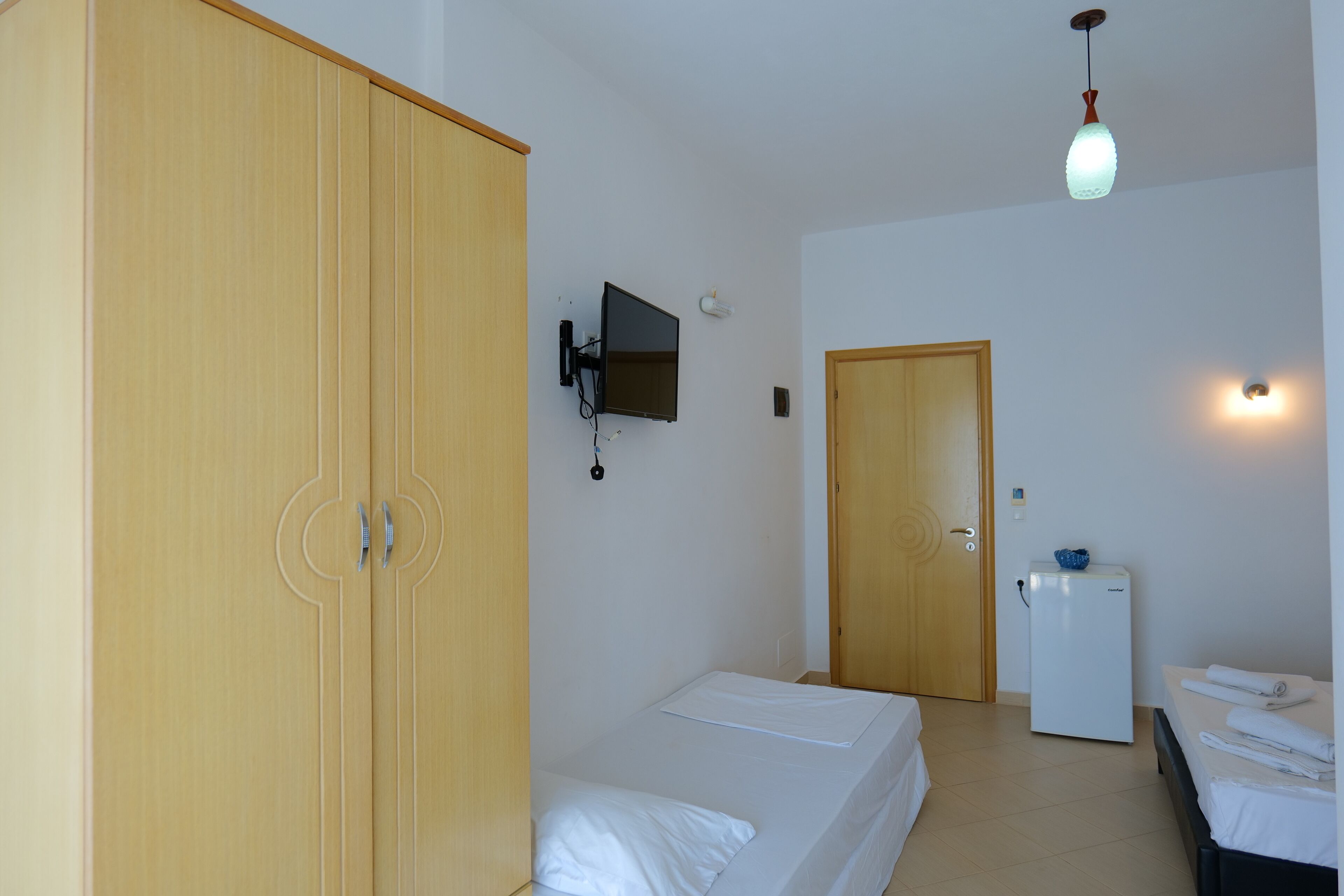 A room with a bed, a wardrobe, a television, a refrigerator, and a door.
