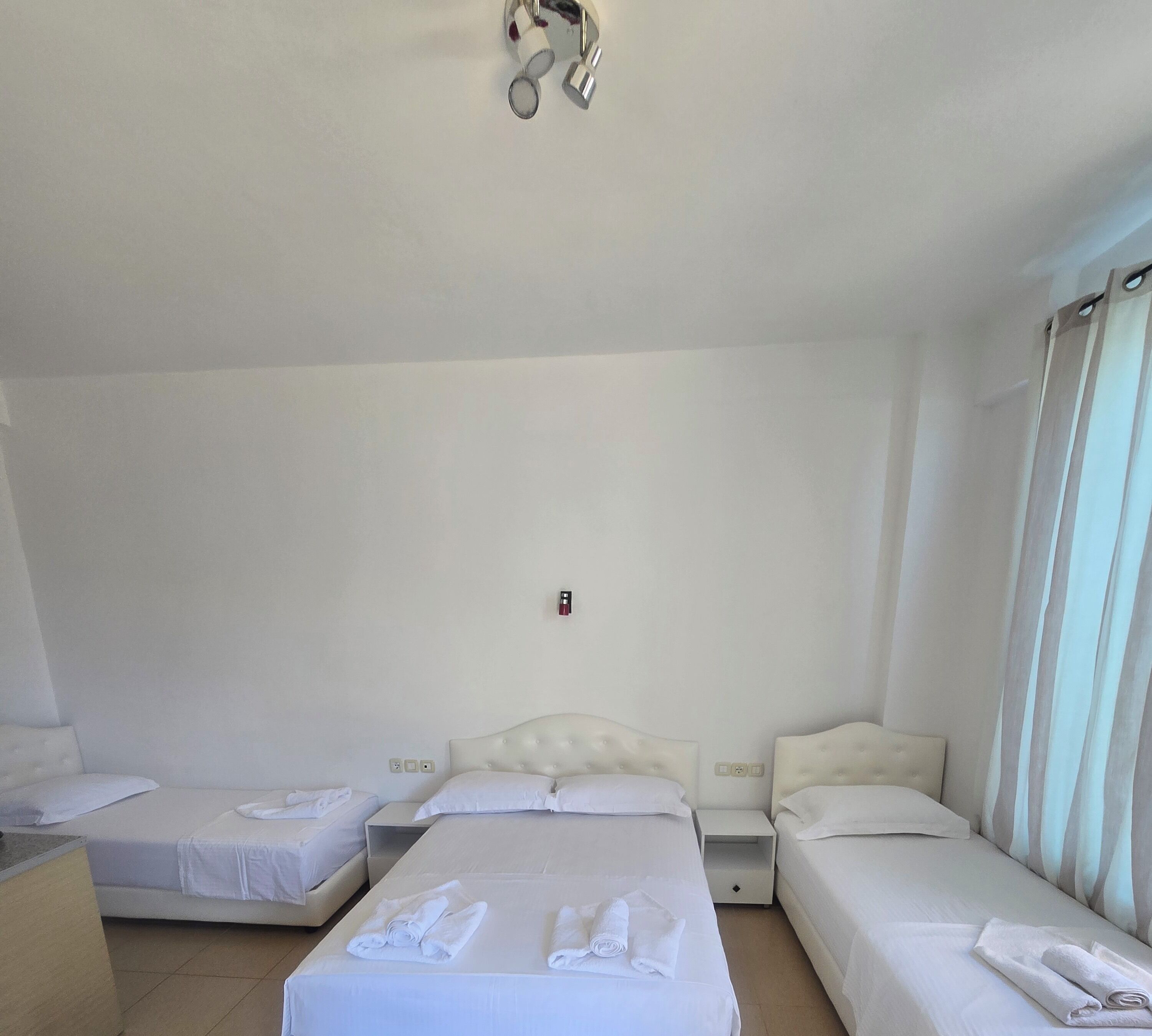 Une chambre d’hôtel avec trois lits, une petite table et un luminaire au plafond.