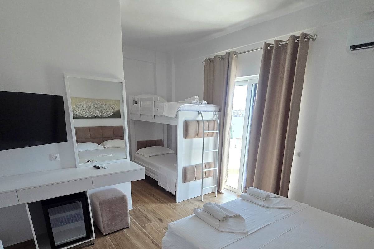 A room with a bunk bed, a desk with a TV, a mirror, and a window with curtains.