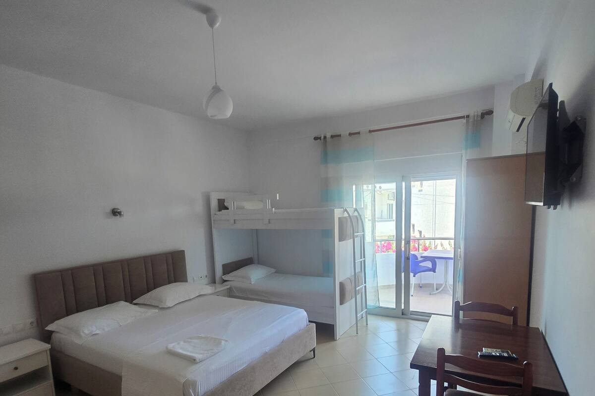 A hotel room with bunk beds, a desk, a chair, a television, and a sliding glass door leading to an outdoor area.