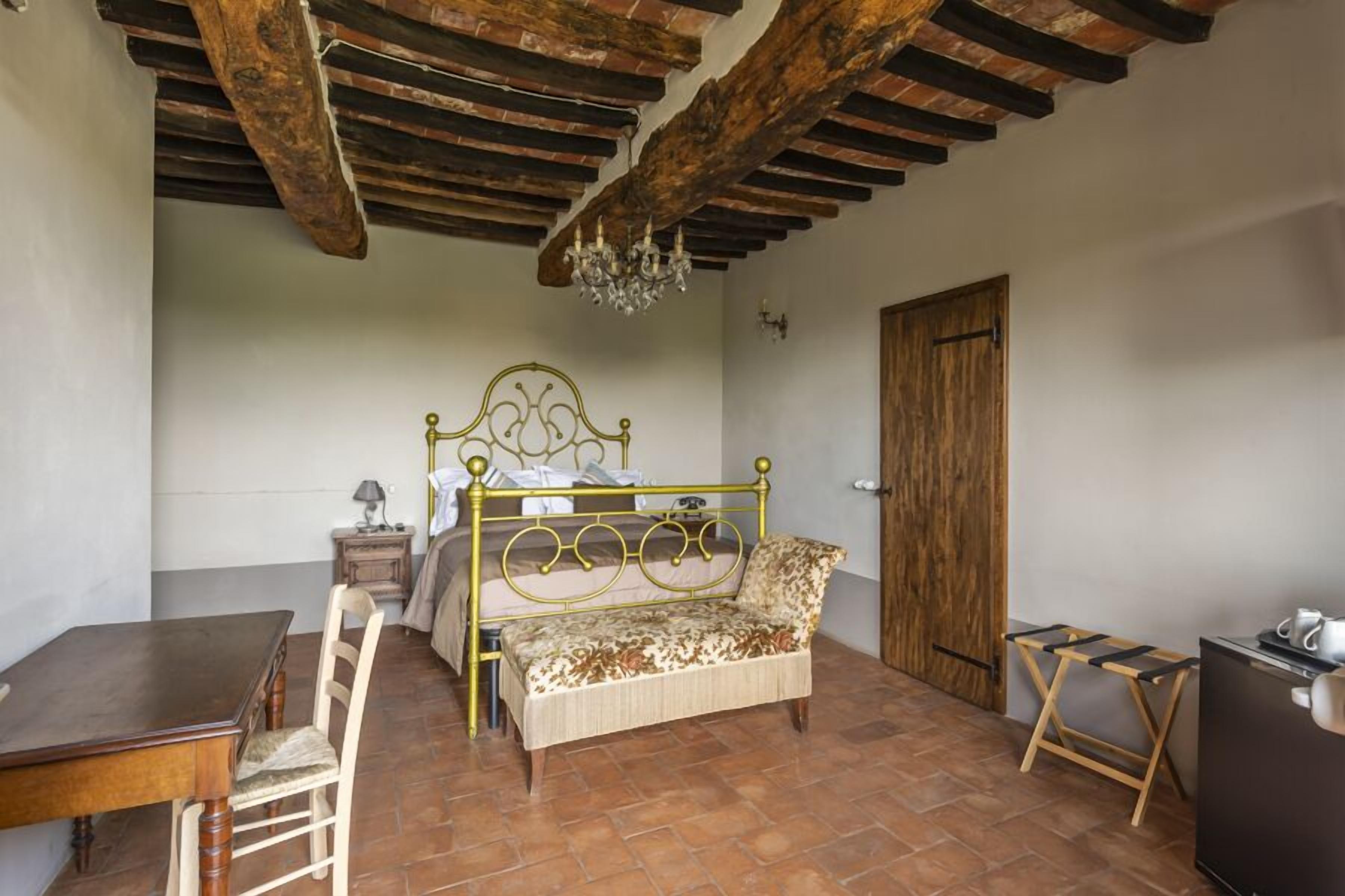 A room with a bed, a wooden table, a chair, a small table with a lamp, and a TV.