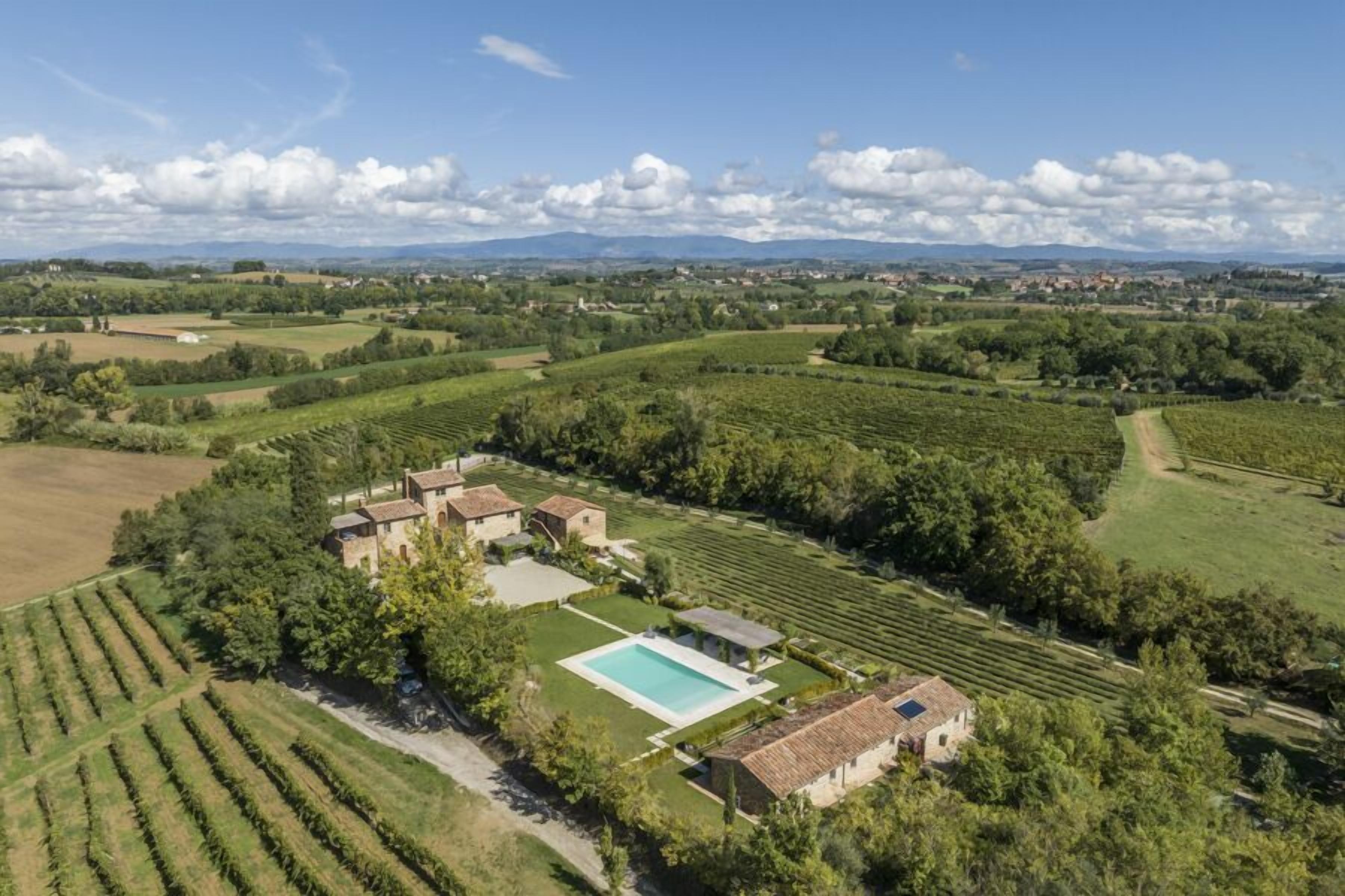 An aerial view of a vineyard estate with terraced fields, a swimming pool, and multiple buildings.