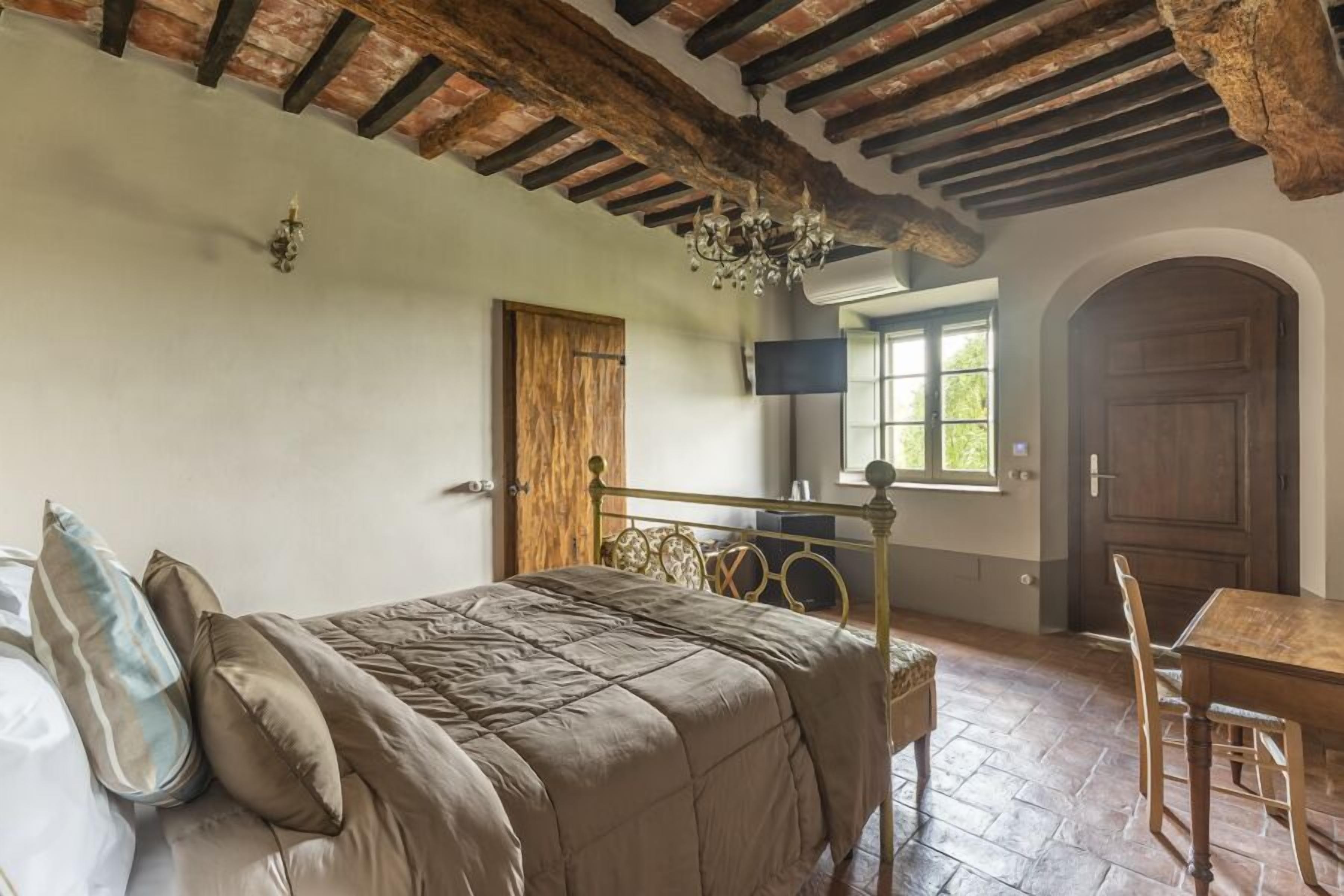 A bedroom with a bed, a wooden table, a TV, and a window.