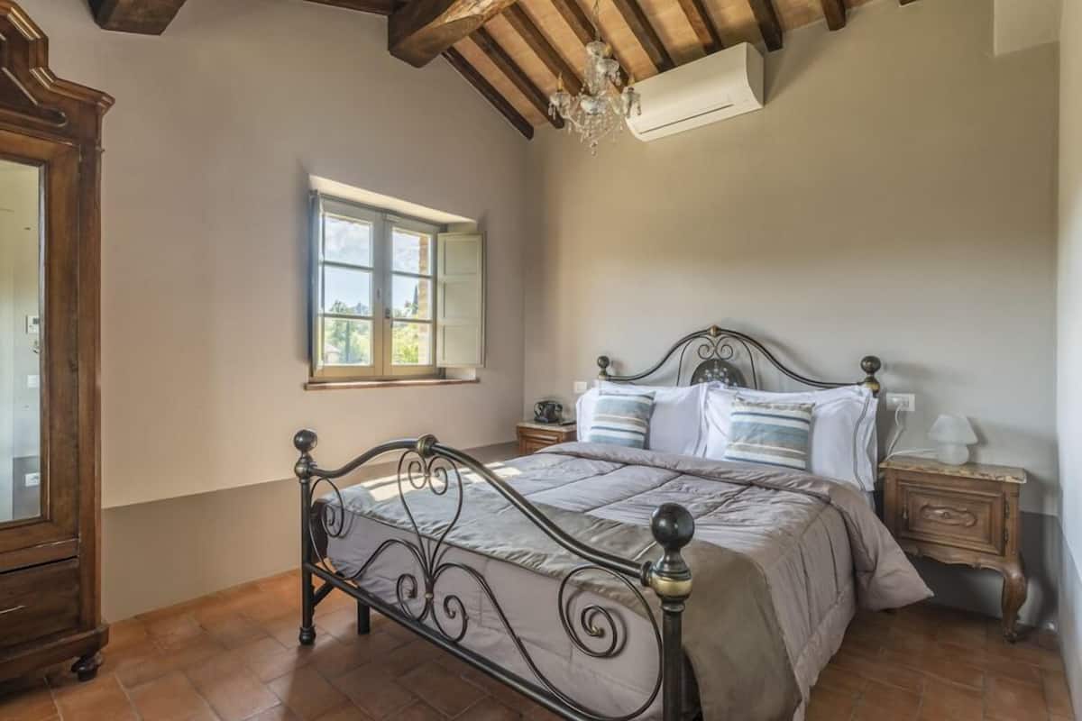 A bedroom with a bed, wooden nightstands, a window, and a chandelier.