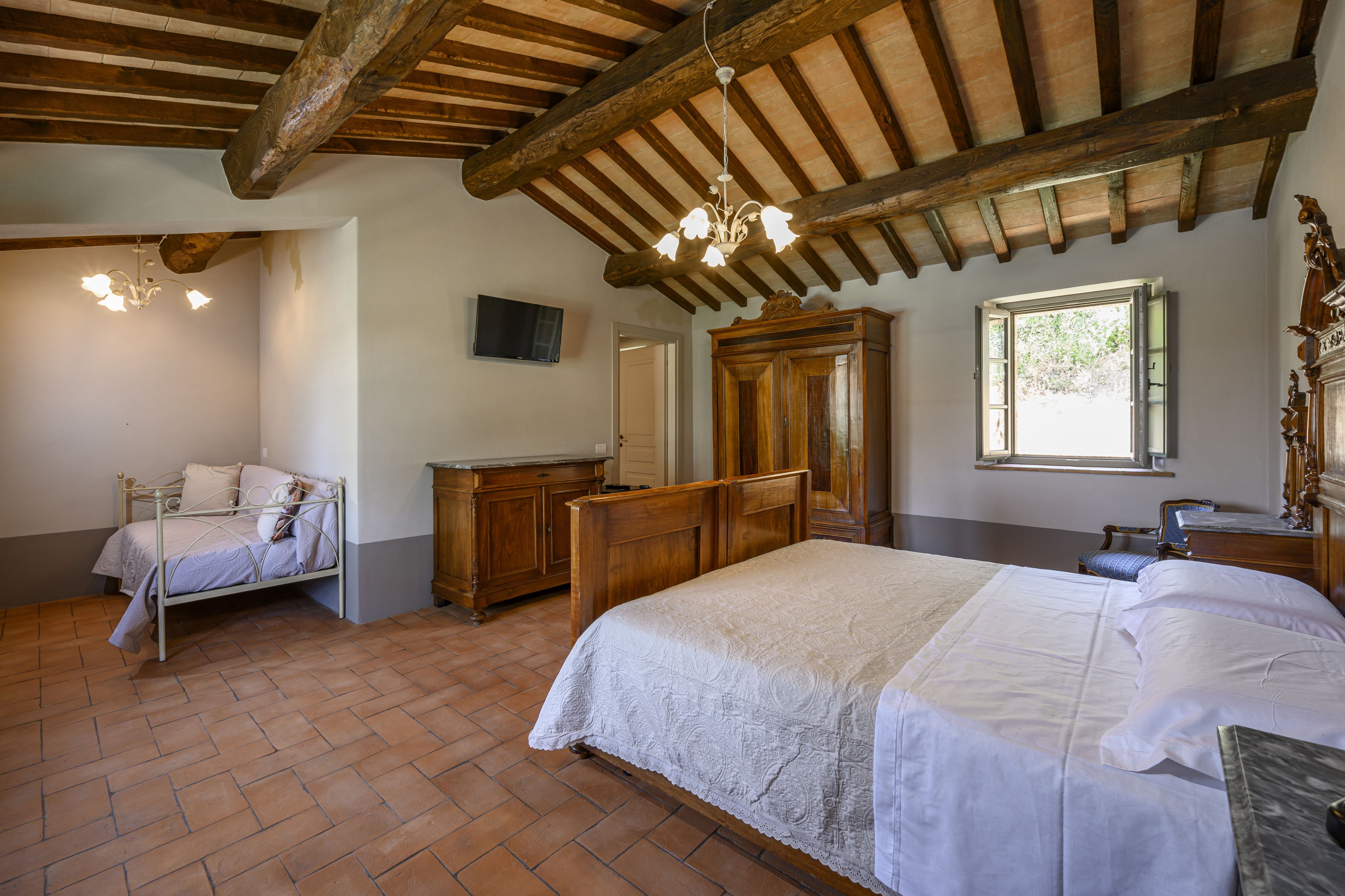 Ein Schlafzimmer mit einem großen Bett, einer Holzkommode, einem an der Wand befestigten Fernseher und einem Fenster.