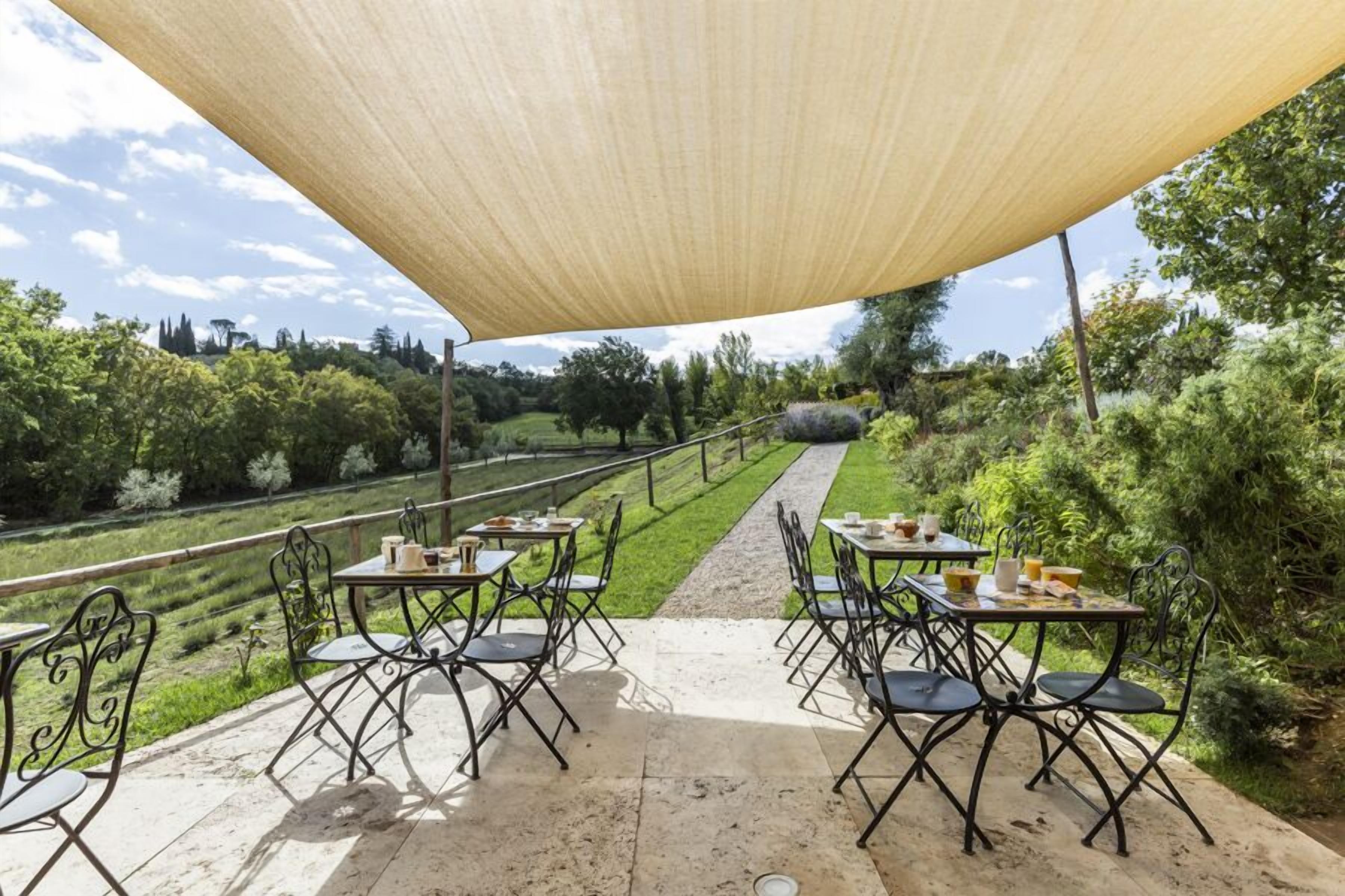 An outdoor patio with tables and chairs, a pathway, and a view of a green landscape.