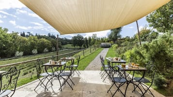 An outdoor patio with tables and chairs, a pathway, and a view of a green landscape.