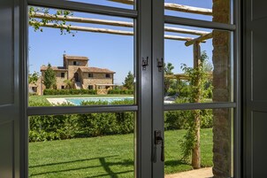 A view through a window of a stone building with a pool, surrounded by greenery.