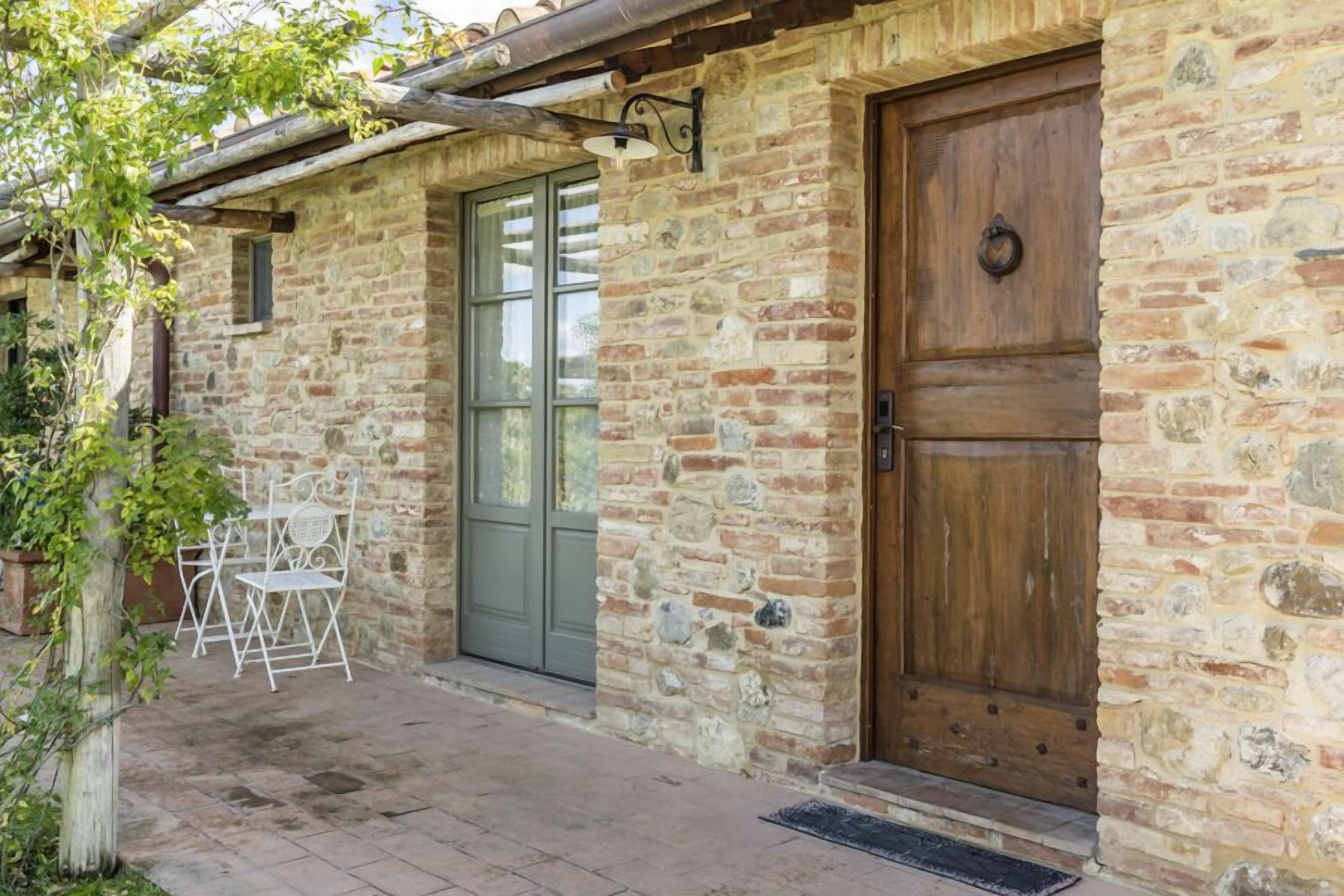 A stone building with a wooden door, a window, and a small outdoor seating area with chairs.