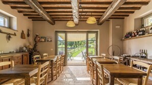 Un comedor rústico con mesas y sillas de madera, suelo de piedra y vistas a un viñedo a través de grandes ventanales.
