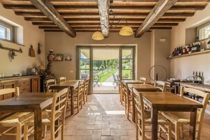 A rustic dining area with wooden tables and chairs, a stone floor, and a view of a vineyard through large windows.