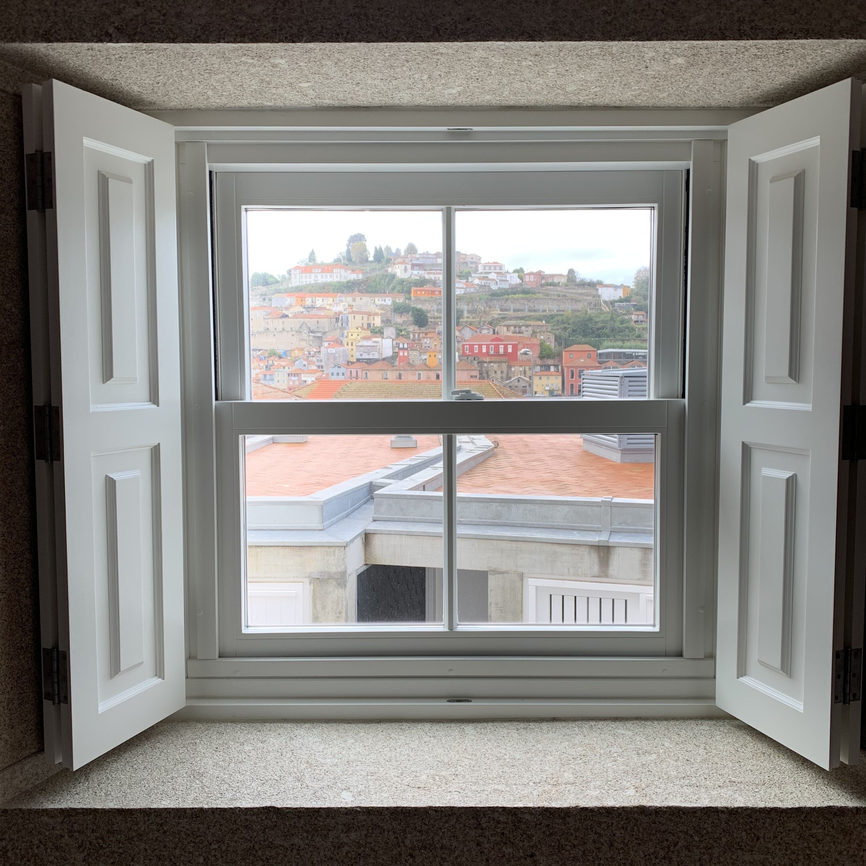 A room with a large window offering a view of a cityscape with buildings and a hill.