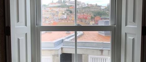 A room with a large window offering a view of a cityscape with buildings and a hill.