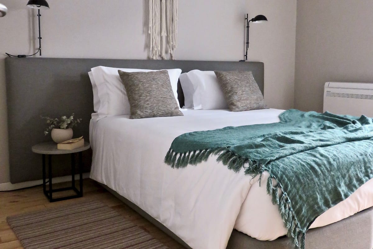 Un dormitorio con cama, mesitas de noche, un tapiz de macramé y aire acondicionado instalado en la pared.
