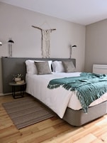 Quarto com cama, mesas de cabeceira, um pendente de macramé e ar condicionado fixado na parede.