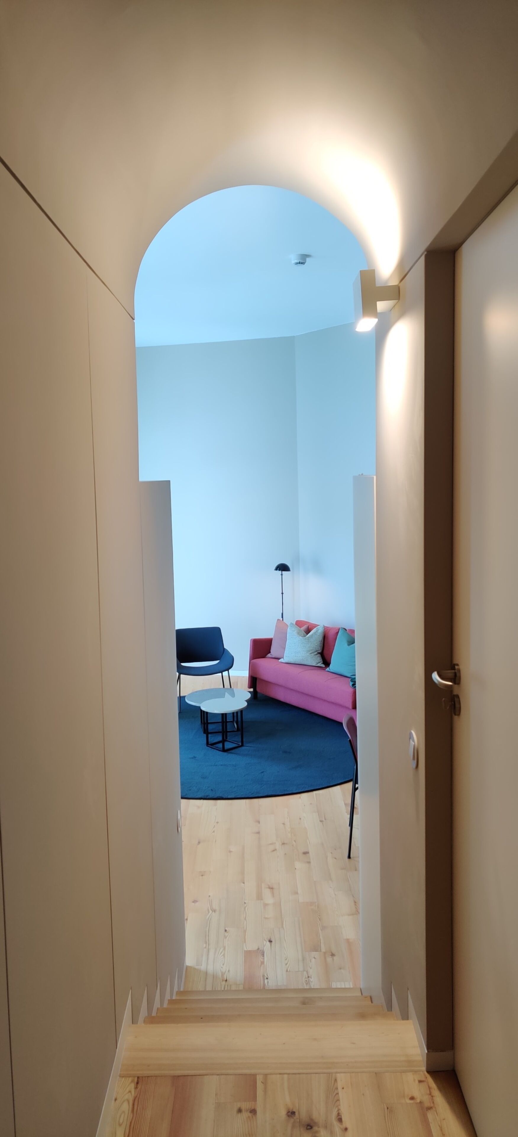 A narrow hallway leading to a living area with a sofa, chairs, and a coffee table.
