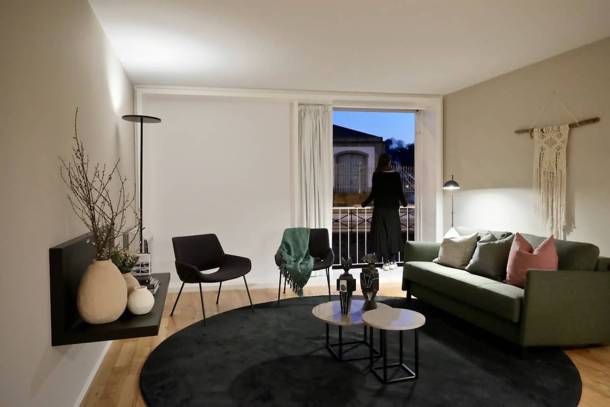 Una sala de estar moderna con un sofá verde, un sillón negro, una mesa de centro redonda y un ventanal con vistas al exterior.