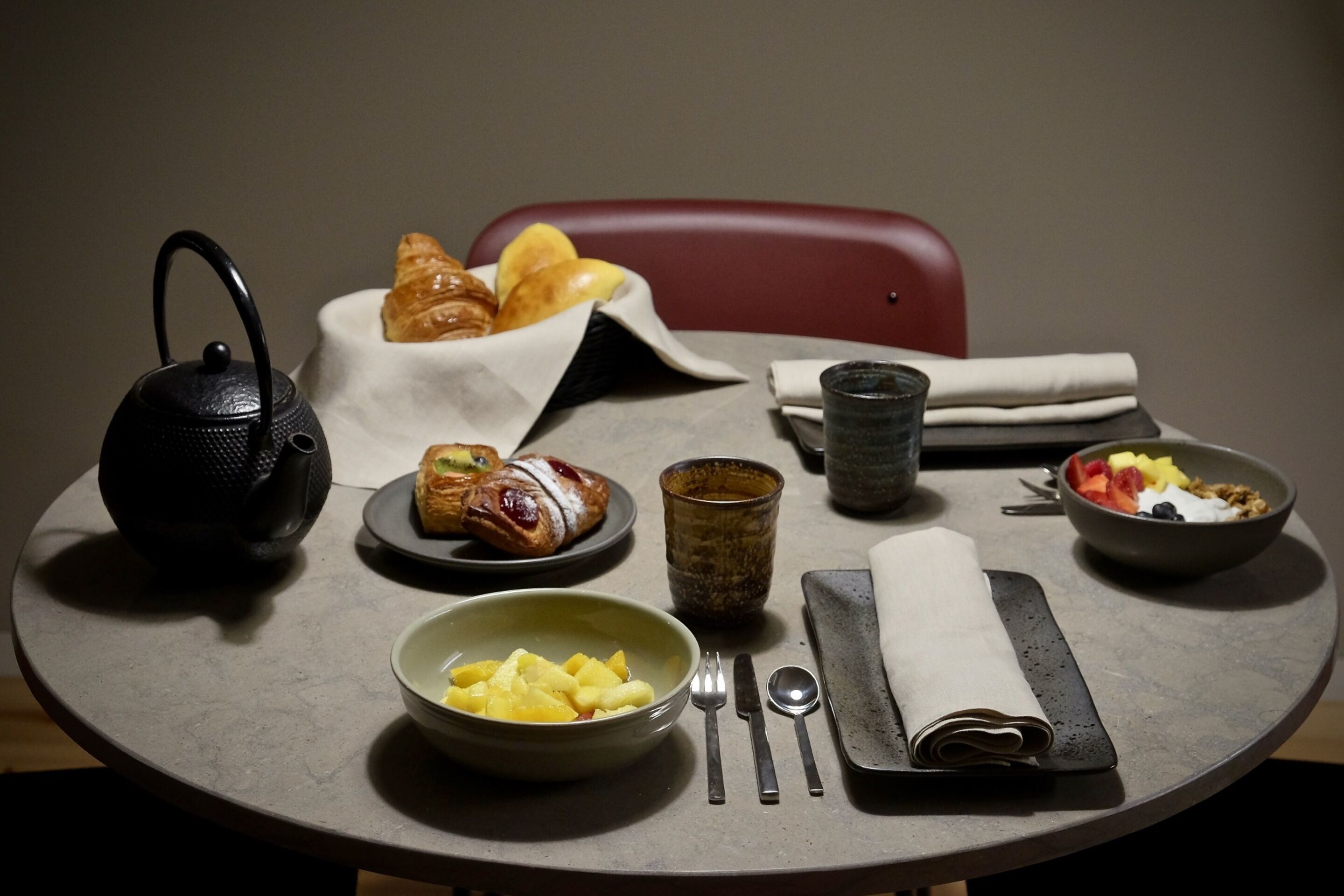 Een gedekte tafel met ontbijtartikelen, waaronder croissants, fruit en een schaal ananas.