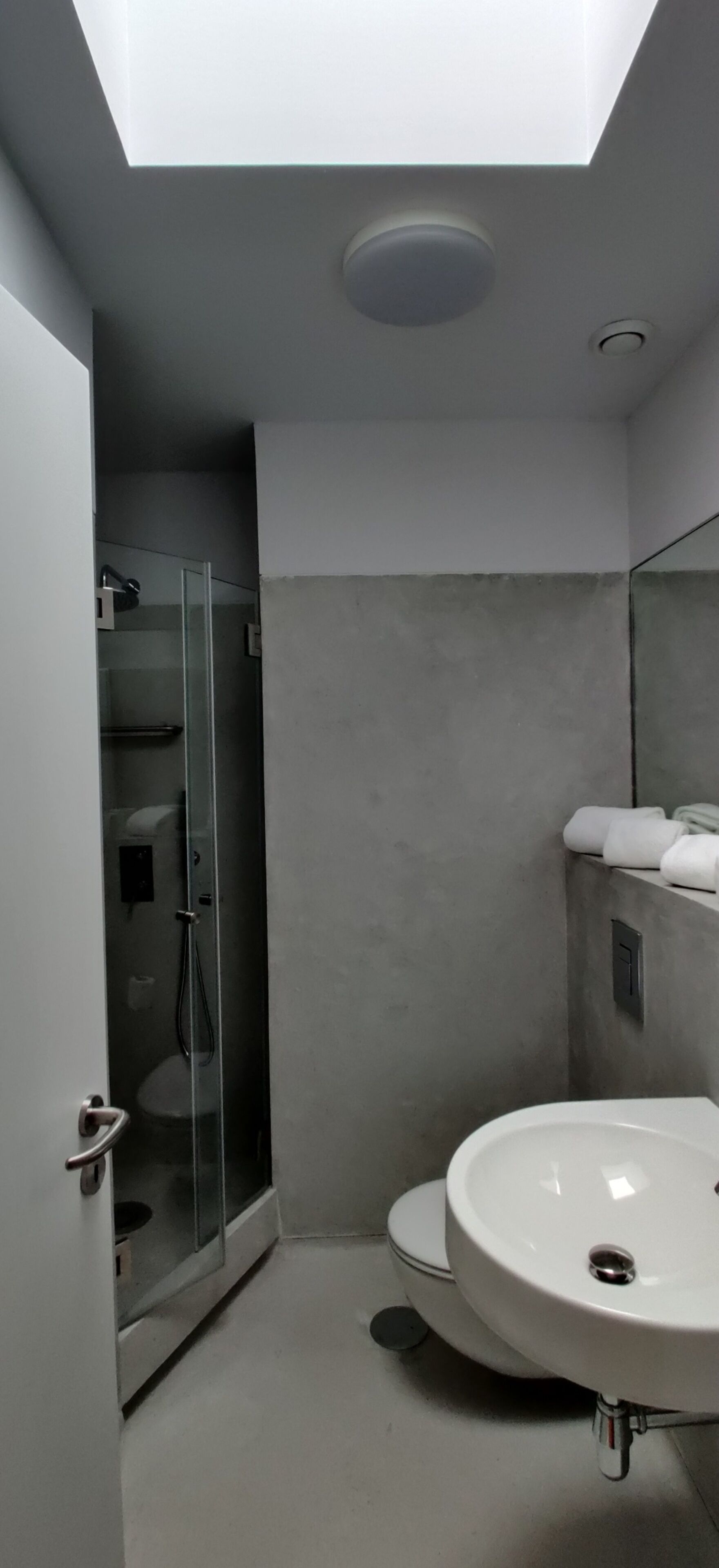 Un baño moderno con tragaluz, cabina de ducha de vidrio, lavamanos blanco y retrete.