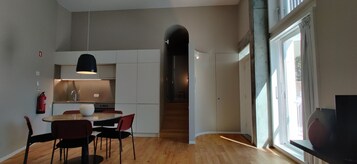 Cozinha moderna com armários brancos, área de jantar com mesa redonda e cadeiras, e uma janela grande que oferece luz natural.