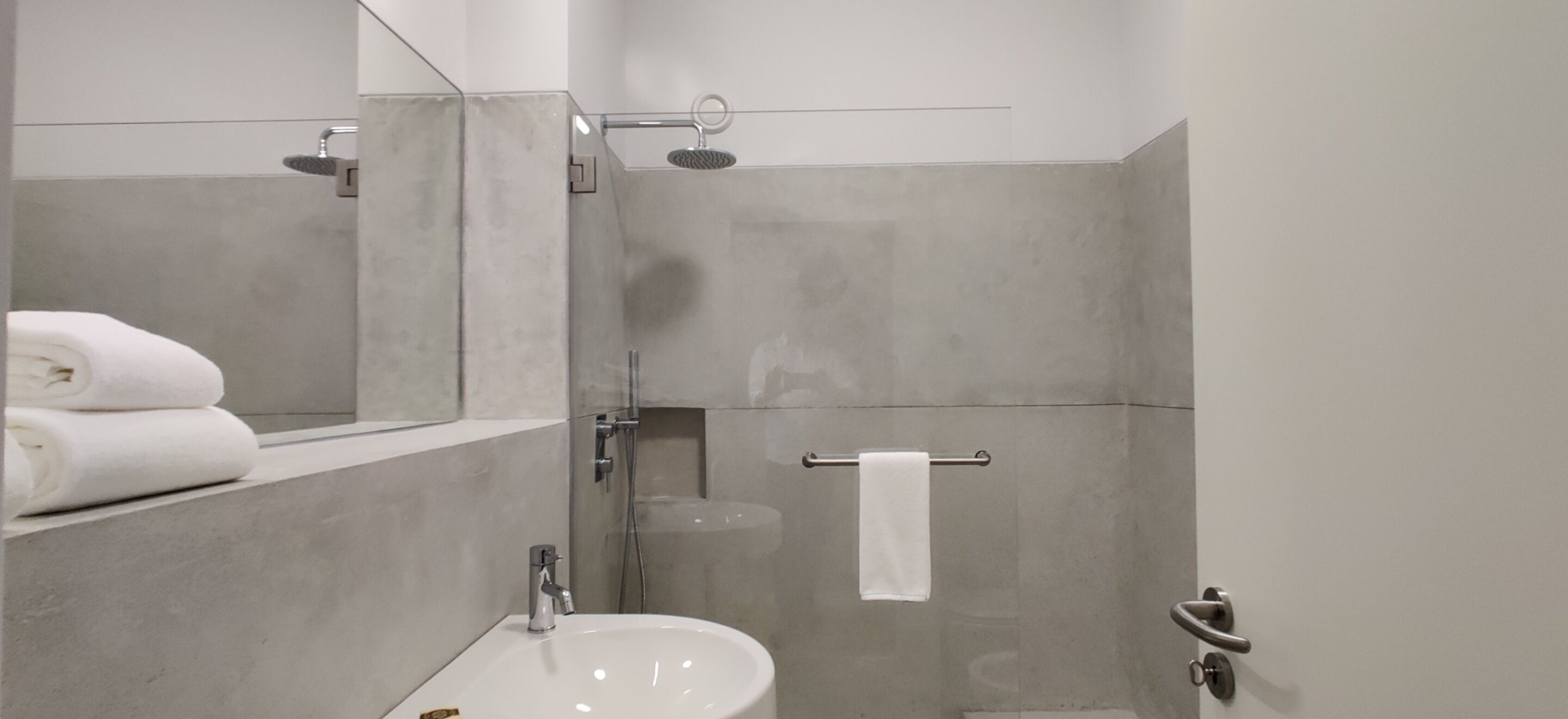 A modern bathroom with a sink, mirror, towel rack, and shower.