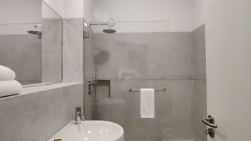 A modern bathroom with a sink, mirror, towel rack, and shower.
