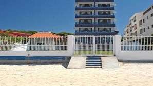 A modern multi-story building with a central staircase, surrounded by a white fence and a pool area. - Flat Bellmare (Florianópolis)