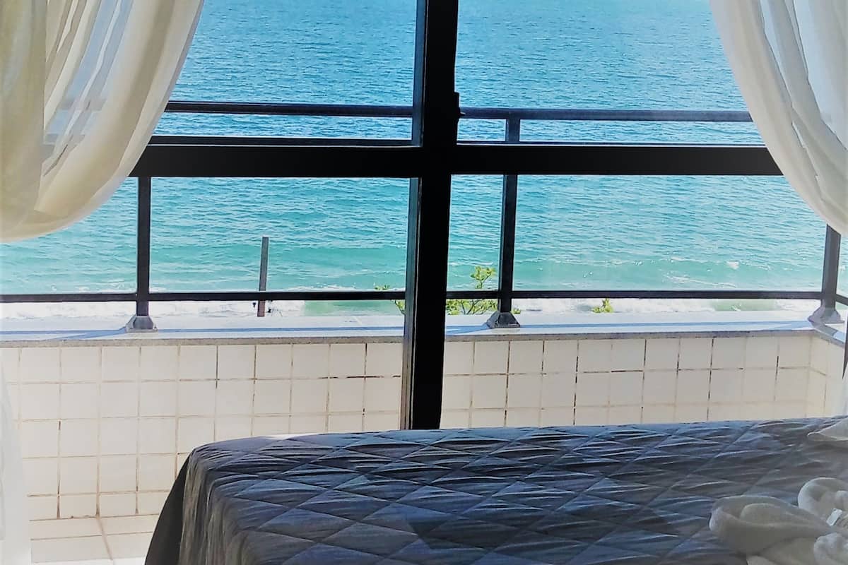 Une chambre à coucher avec un lit, une vue sur la mer et des rideaux.