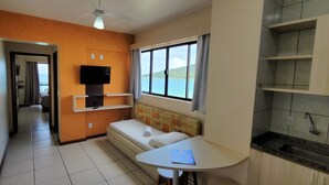 A compact room with a TV, a small table, a sofa, and a window with a view. - Flat Bellmare (Florianópolis)
