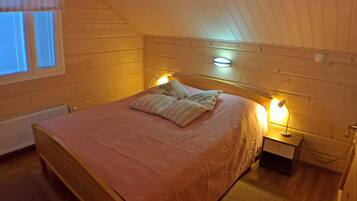 Un dormitorio acogedor con techo inclinado, una cama con colcha rosa, dos lámparas de noche y una ventana con persianas.