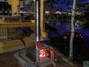 Un poêle à bois avec une cheminée, installé devant une terrasse en bois et donnant sur une étendue d'eau.