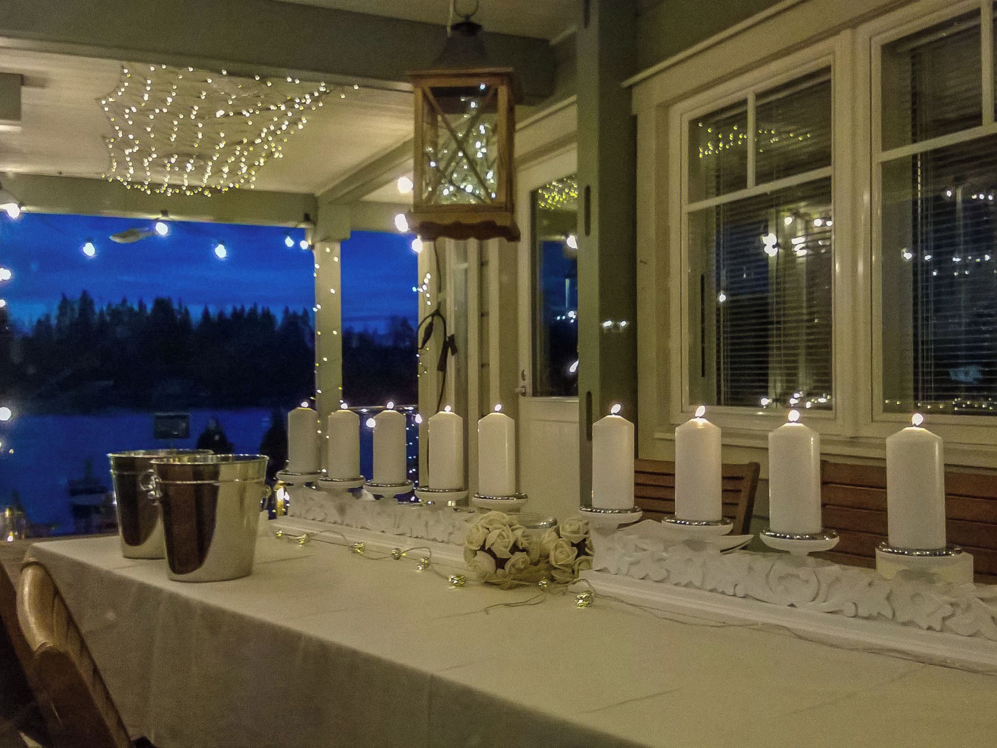 A table set with candles and a decorative centerpiece, with a view of trees and a building in the background.