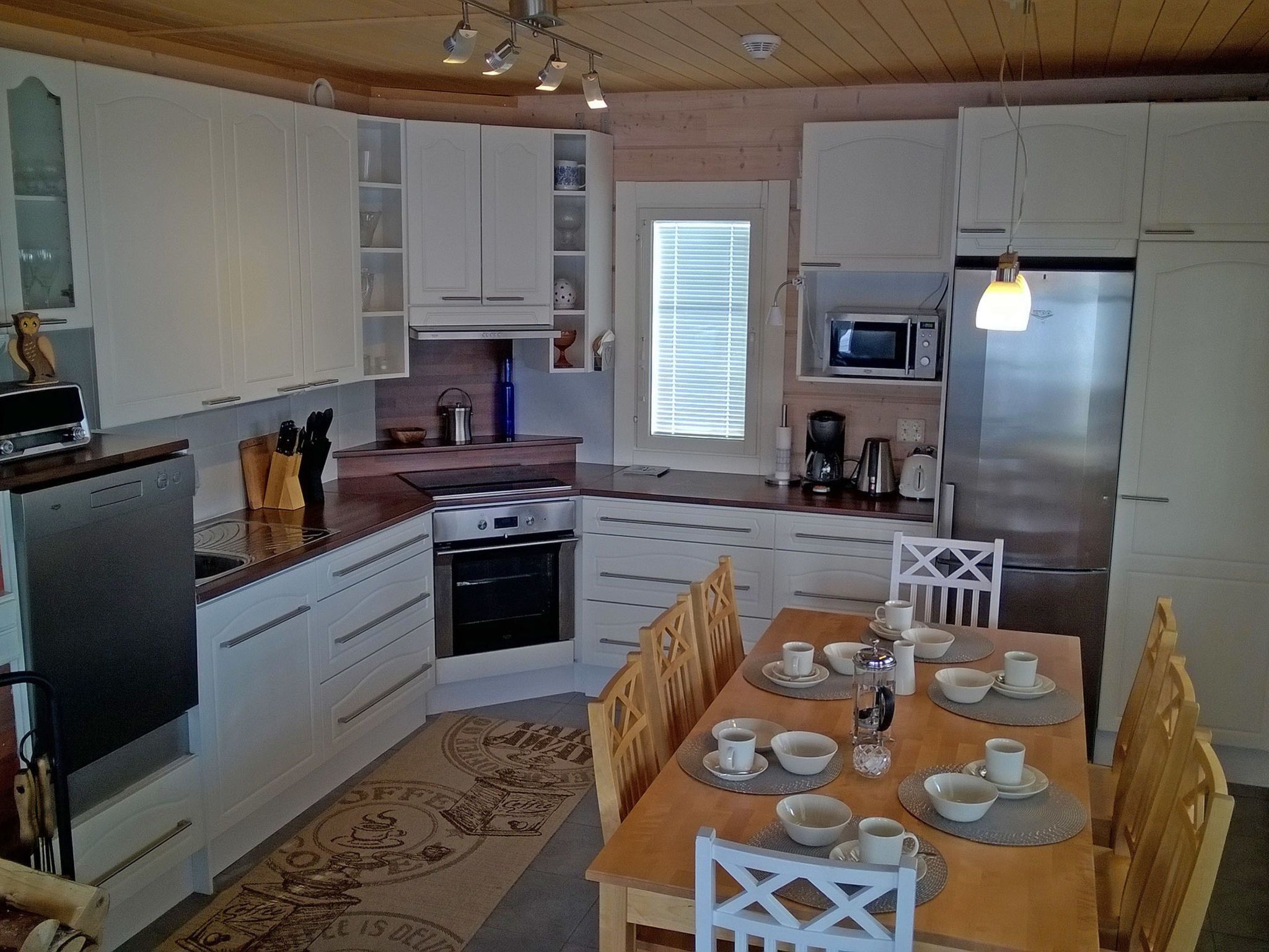 Une cuisine moderne avec des meubles blancs, une table à manger pour quatre personnes et un réfrigérateur.