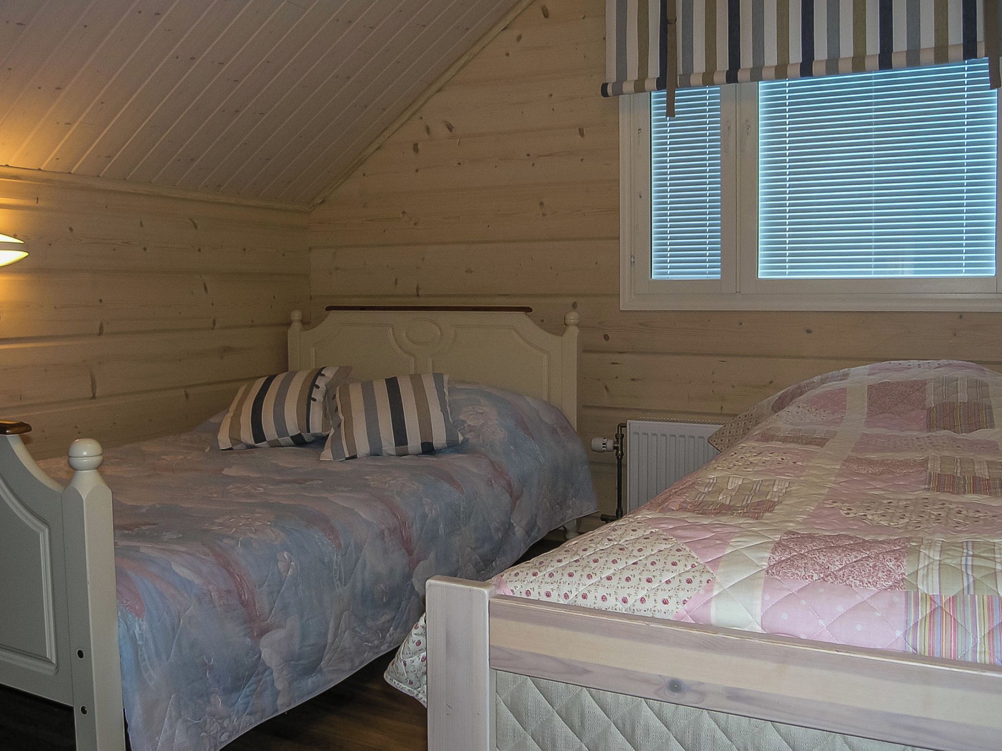 A bedroom with two beds, a sloped ceiling, and a window with blinds.