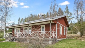 Punainen puinen mökki, jossa on kuisti ja pienet portaat, jotka johtavat ylös mökkiin.