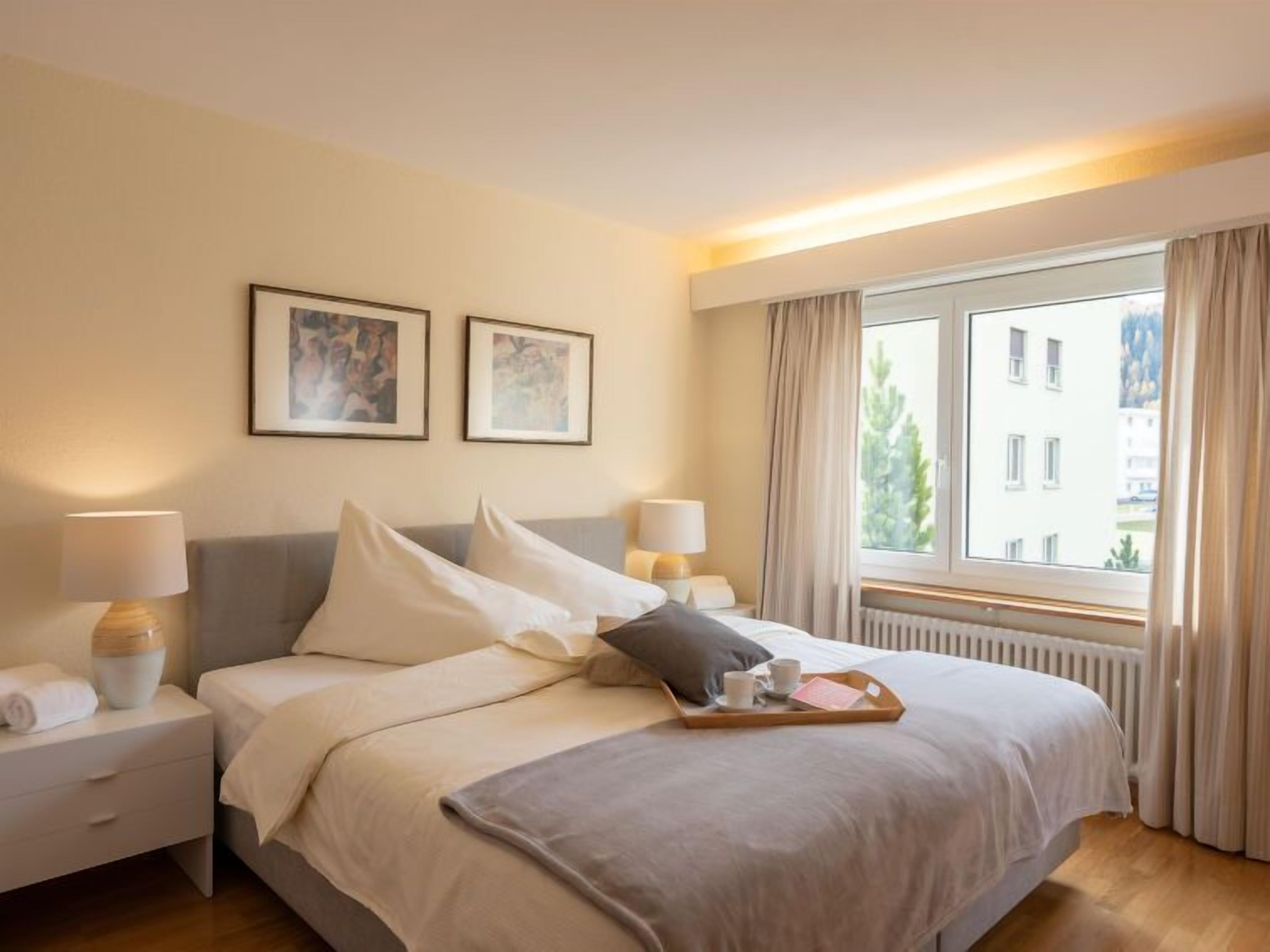 Ein Hotelzimmer mit Bett, Nachttischen, einem Fenster mit Vorhängen und zwei gerahmten Bildern an der Wand.