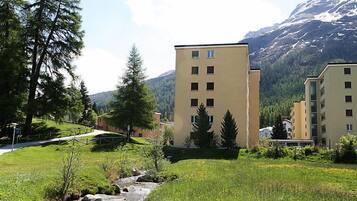 Il s’agit d’un quartier résidentiel traversé par un petit ruisseau, avec de l’herbe verte et des arbres. On y trouve des bâtiments dotés de nombreuses fenêtres, et une montagne se profile à l’arrière-plan.