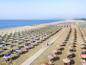 A beach with rows of umbrellas and chairs, a clear sky, and the ocean in the background.