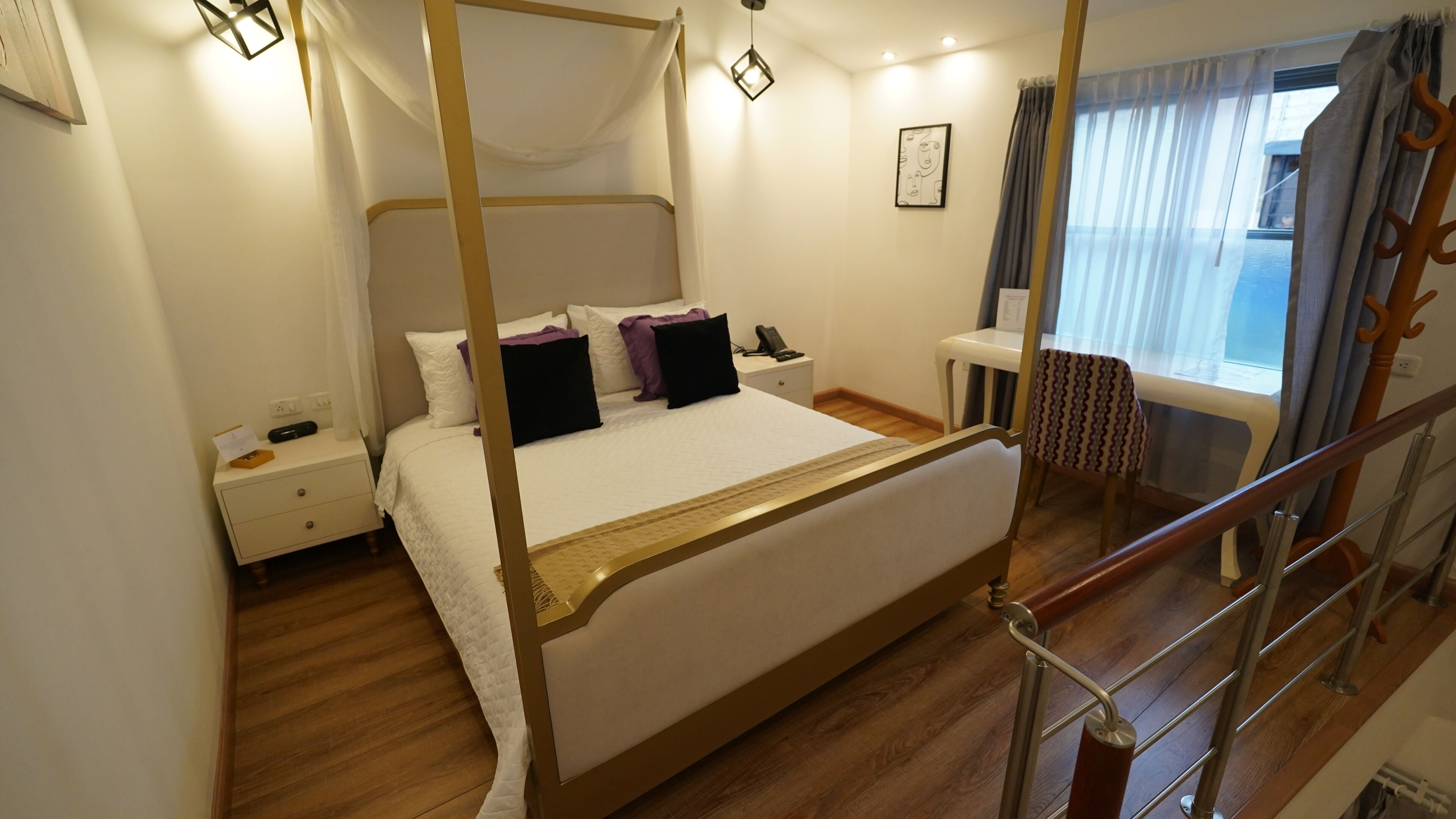 Una cama con dosel y cuatro columnas, una mesita de noche con un teléfono, y una ventana con cortinas.