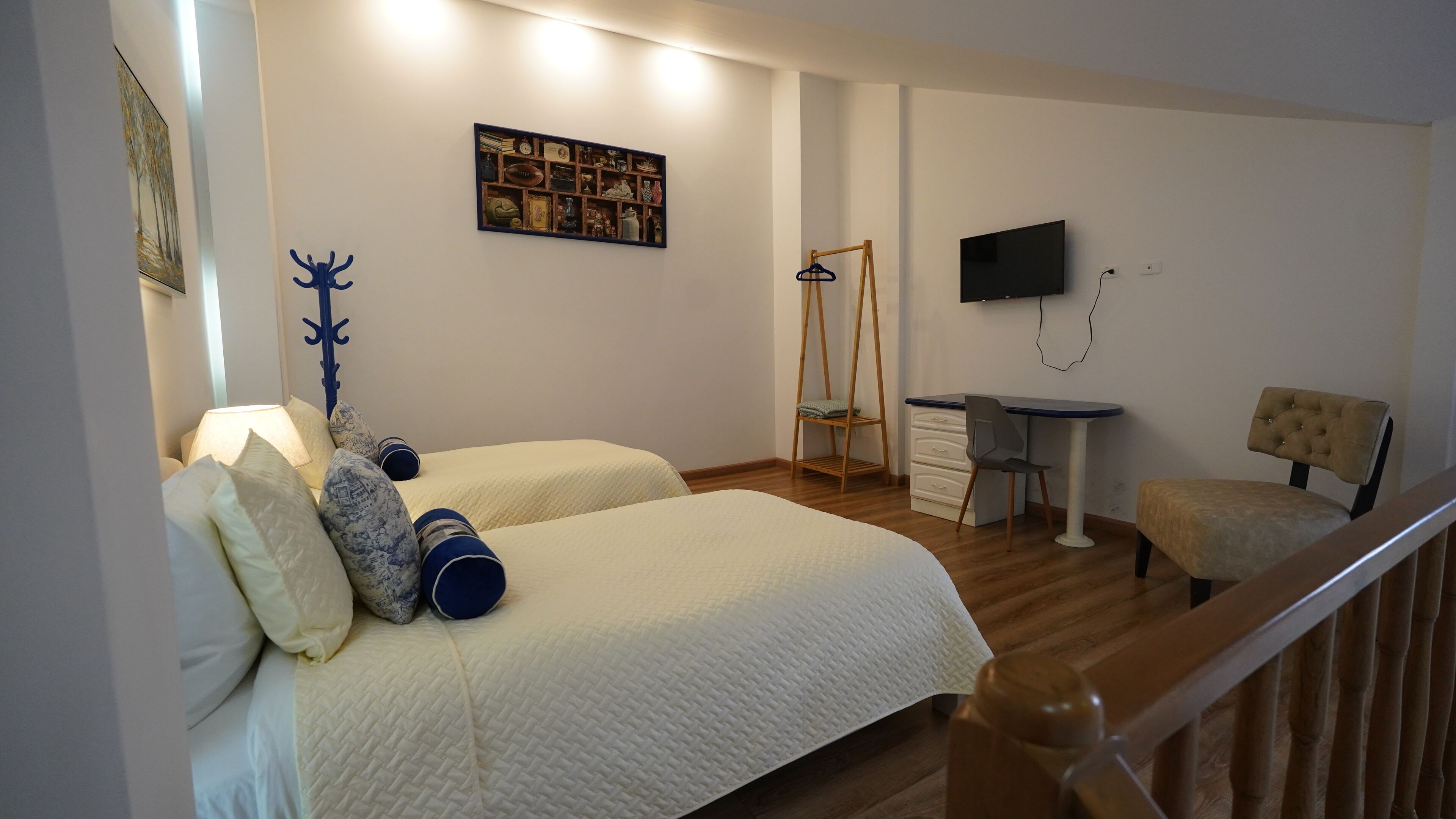 A hotel room with two beds, a desk, a chair, a TV, and a wooden railing.