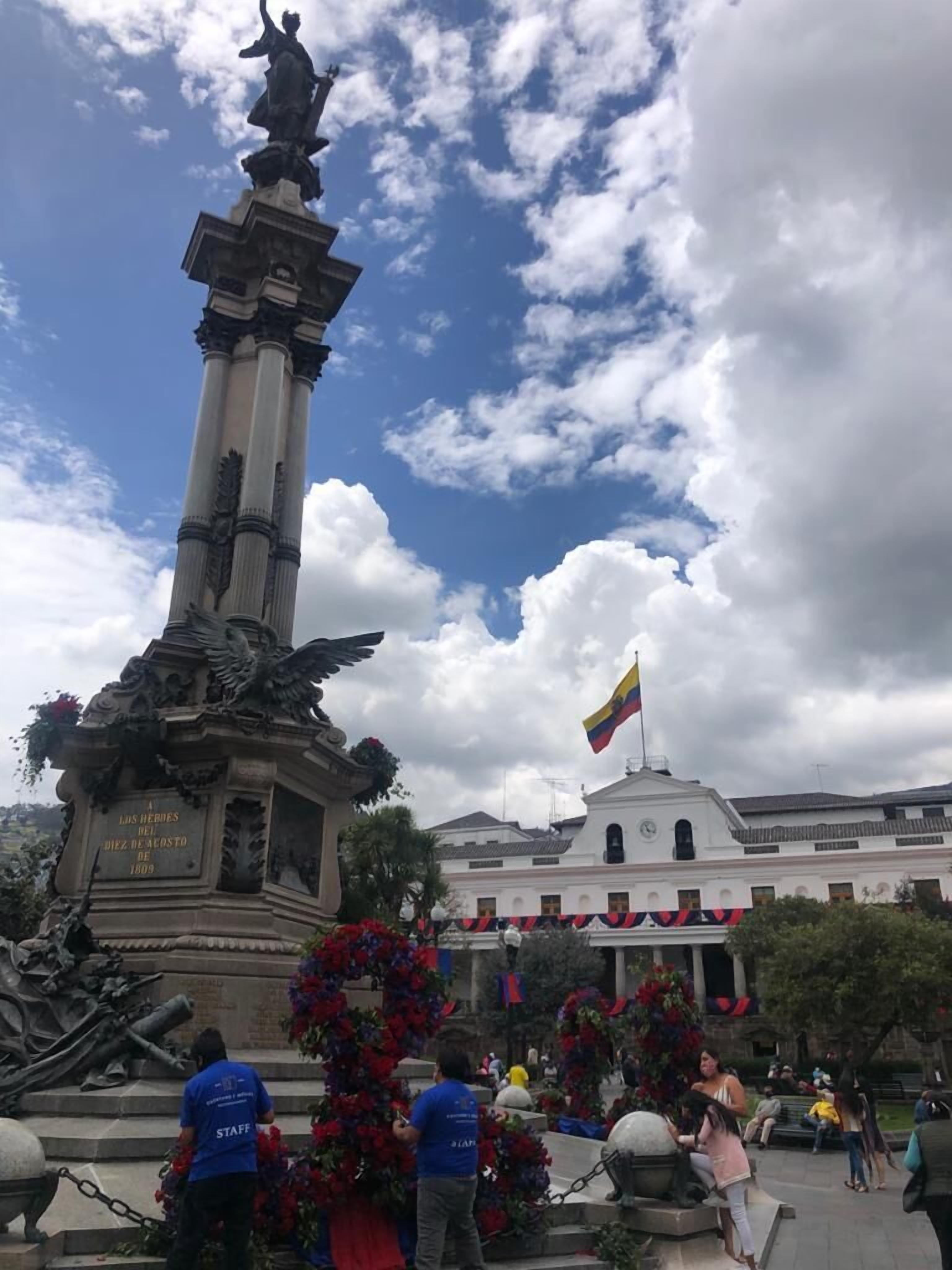 Un monumento con inscripciones, una bandera y un edificio al fondo.