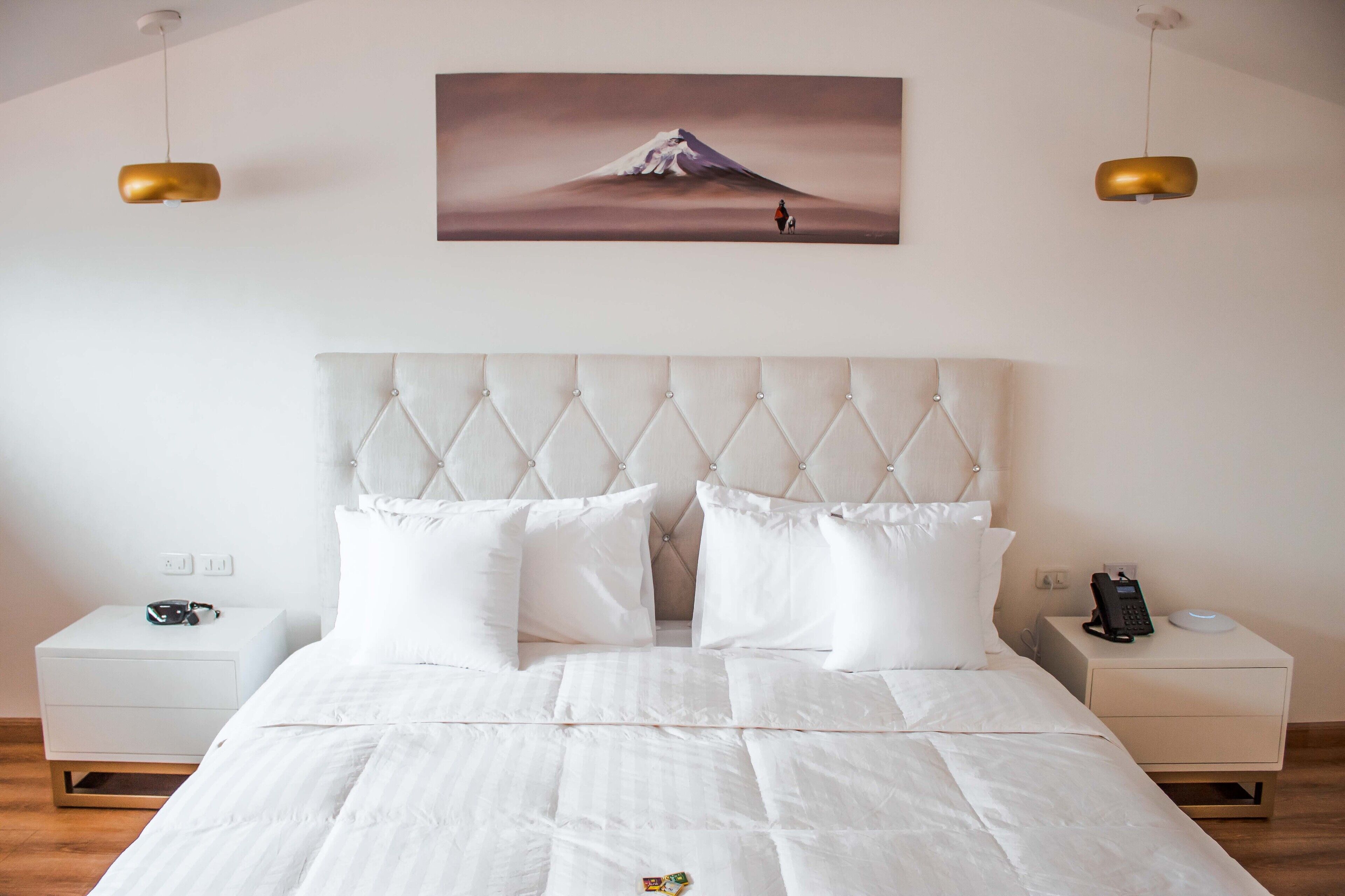 A neatly made bed with a tufted headboard, white bedding, and two bedside tables with a phone and a lamp on each.