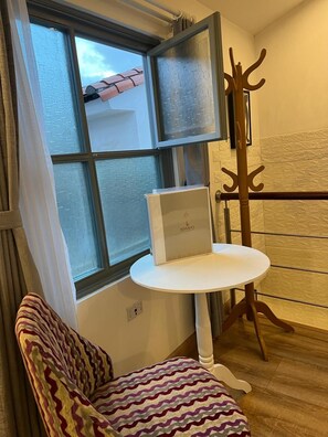 A corner room with a window, a white table, a patterned chair, and a coat rack. - Adamas House Hotel (Quito)