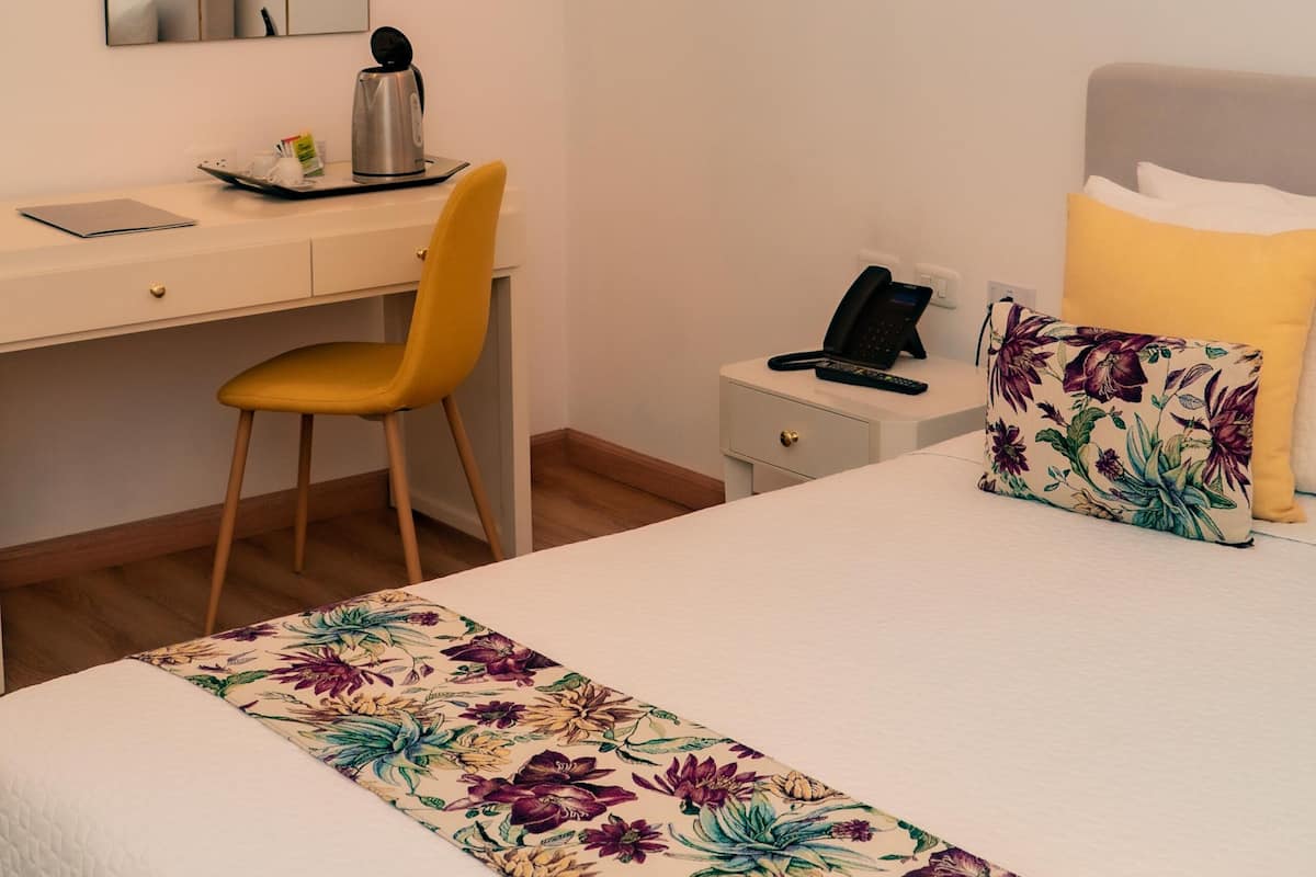 Ett hotellrum med en säng, ett skrivbord, en stol, ett nattduksbord och en spegel.