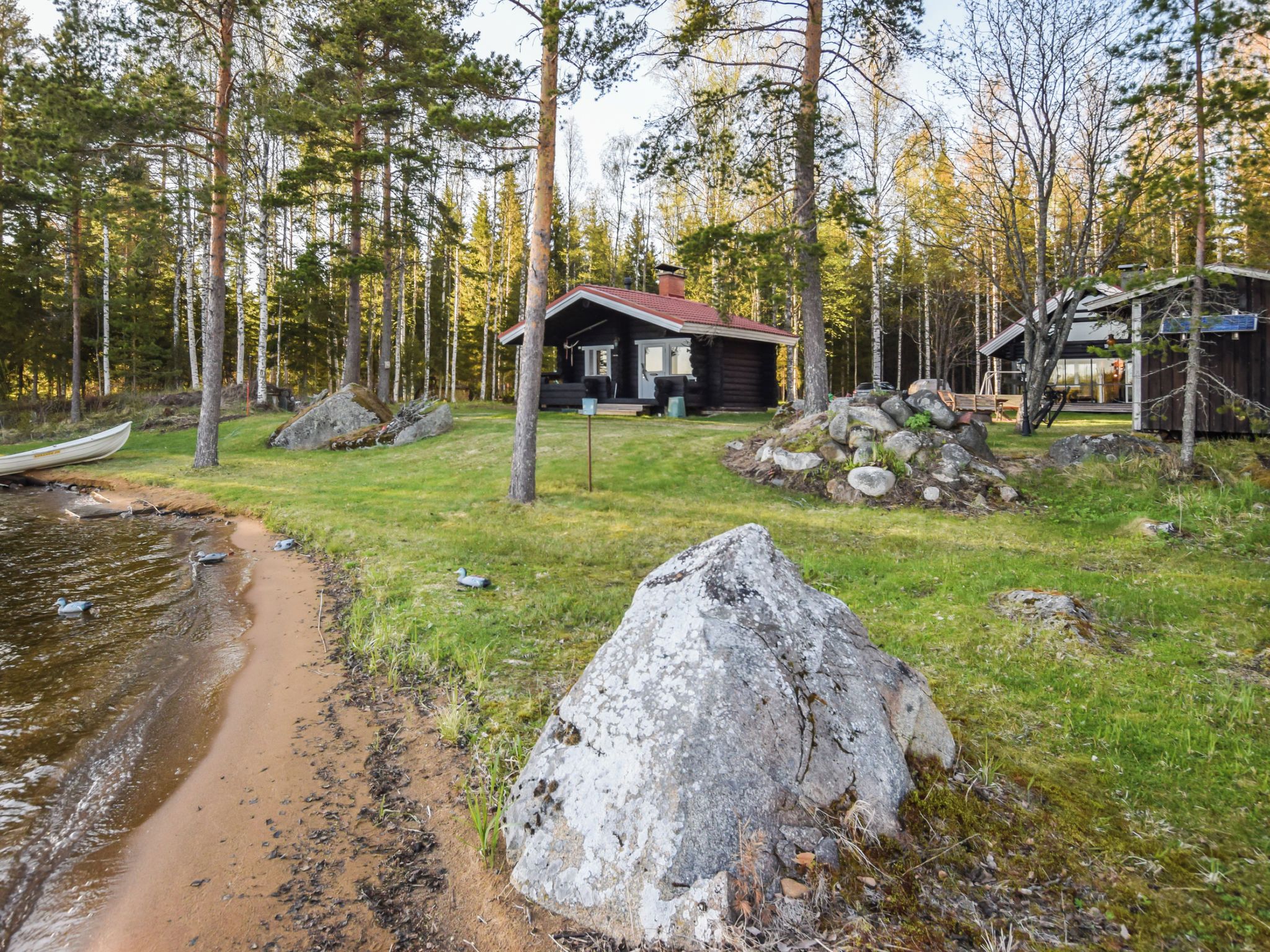 Une cabane dotée d’un porche, entourée d’une forêt, d’un petit quai et d’un amas de rochers.