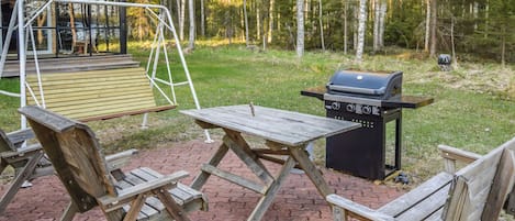 A wooden outdoor seating area with benches and a table, a barbecue grill, and a swing set.